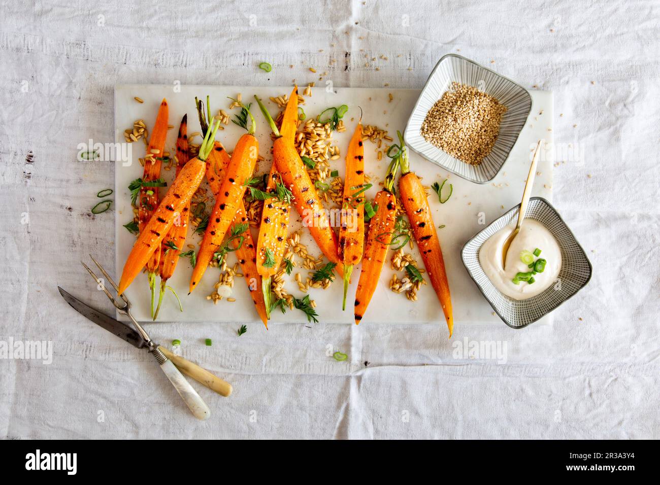 Carote grigliate con farro, cipolline, foglie di carote, semi di sesamo e una salsa di yogurt Foto Stock