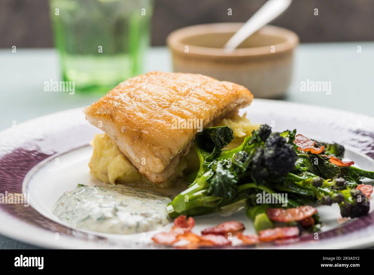 Pesce fritto su un letto di purè di patate con broccolini e salsa alle erbe Foto Stock