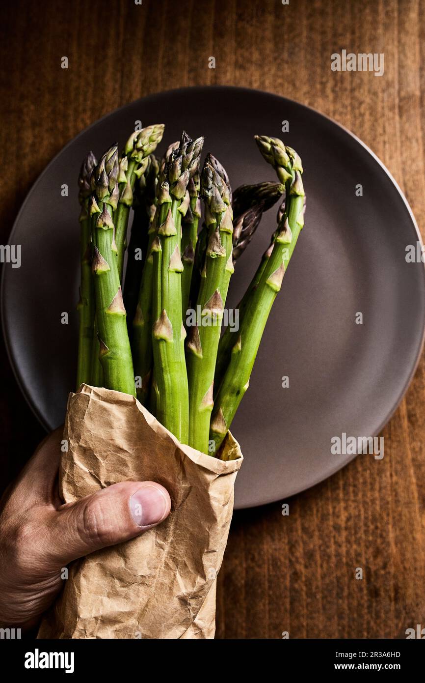 Mano che tiene un fascio di asparagi verdi freschi in un sacchetto di carta Foto Stock