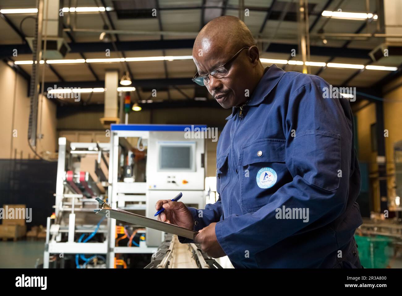 Supervisore nero africano maschio che controlla una clipboard su una linea di assemblaggio di un impianto di imballaggio Foto Stock