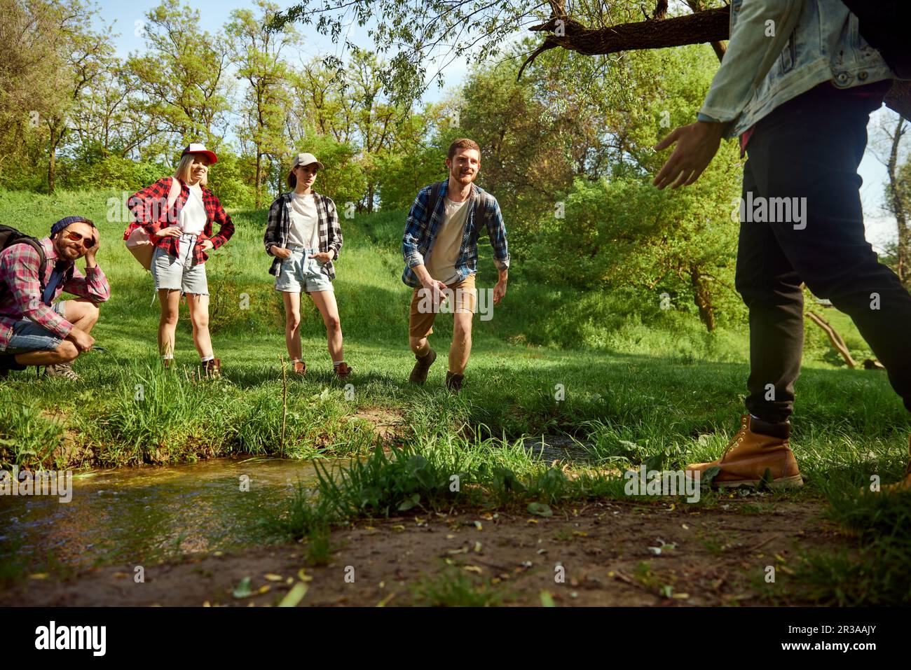 Divertendoti. Gruppo di amici, giovani attivi che vanno a piedi, a piedi nella foresta, saltando sul fiume in caldo giorno di primavera Foto Stock