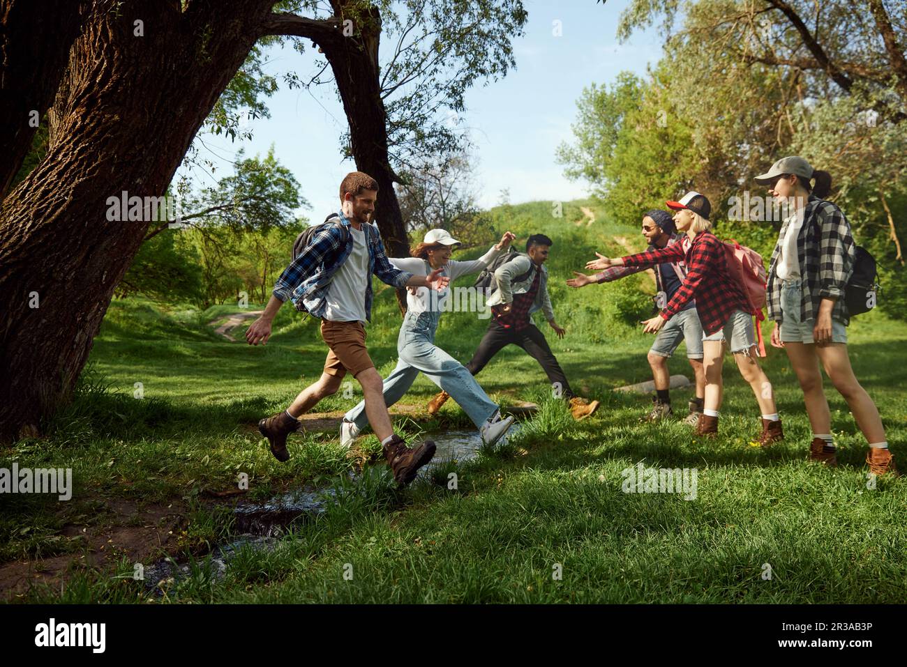 Amici, giovani attivi fare escursioni, camminare nella foresta, saltare sul fiume in caldo giorno di primavera. Tempo libero attivo Foto Stock