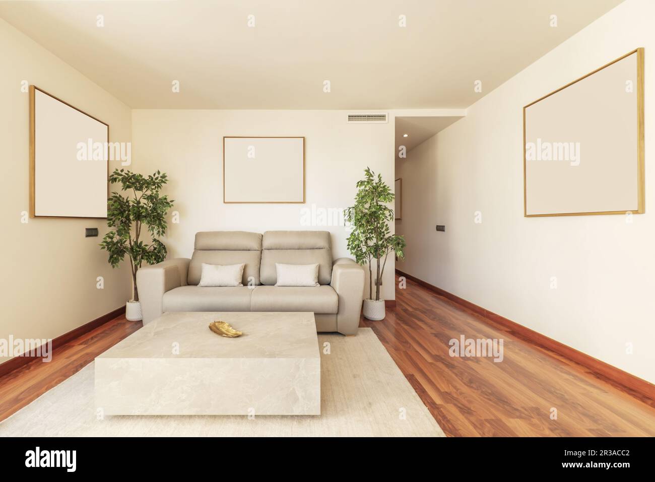 Soggiorno di una casa vacanze decorata con tonalità chiare, tappeto beige, un divano grigio a due posti e piante decorative di plastica Foto Stock