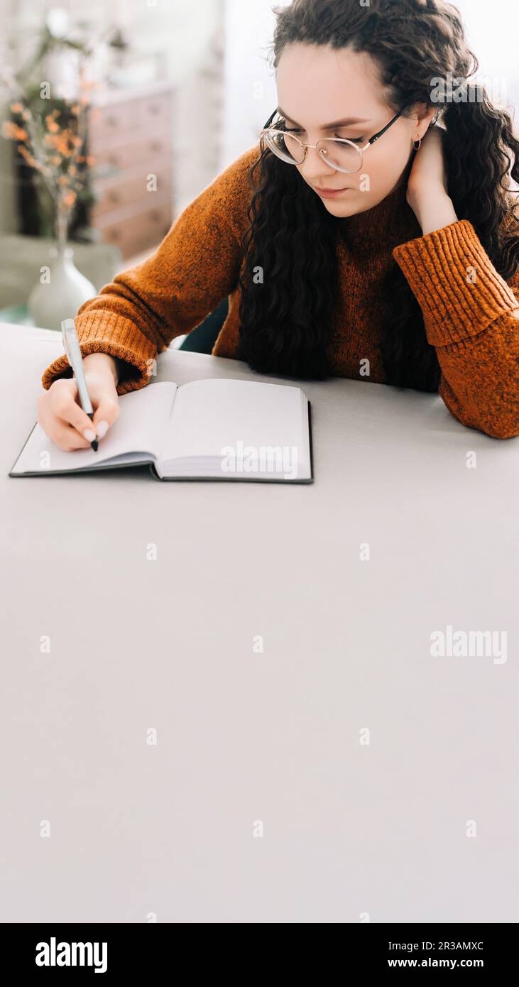 Giovane donna multitasking: Scrivere in rivista e studiare per il successo. Vista ravvicinata della donna che scrive nel copybook per studiare o fare la lista di controllo. FO Foto Stock