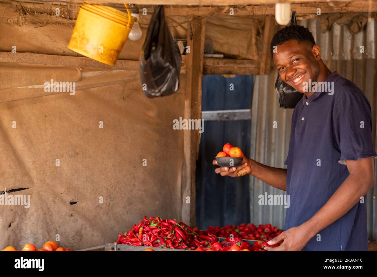 giovane bel commerciante locale africano sentirsi felice come lui organizza i pomodori per la vendita. Foto Stock