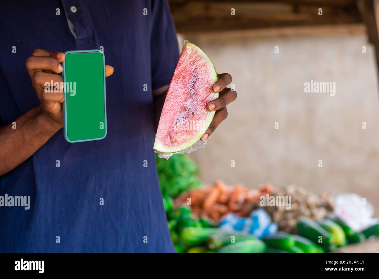 copia l'immagine spaziale di un giovane commerciante africano maschile che detiene anguria e smartphone con schermo verde vuoto in un tipico mercato africano locale. Foto Stock