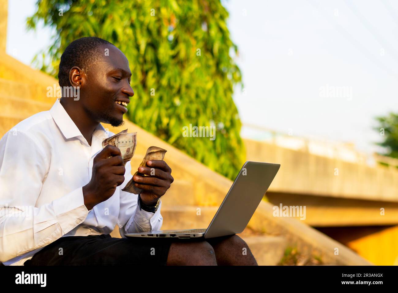 Felice uomo d'affari seduto con il suo notebook e contando un sacco di denaro. giorno di paga della transazione commerciale riuscita Foto Stock