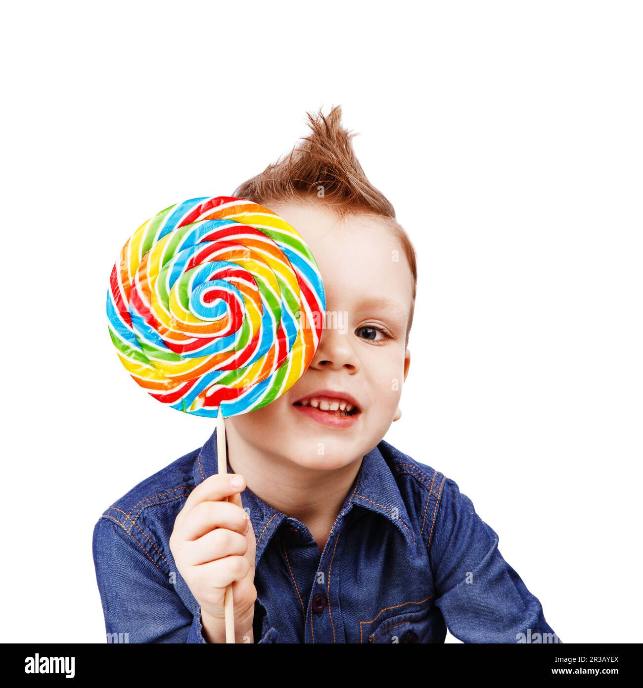 Un ragazzo in una camicia in denim che mangia lecca. Felice capretto con una caramella grande isolata su sfondo bianco Foto Stock