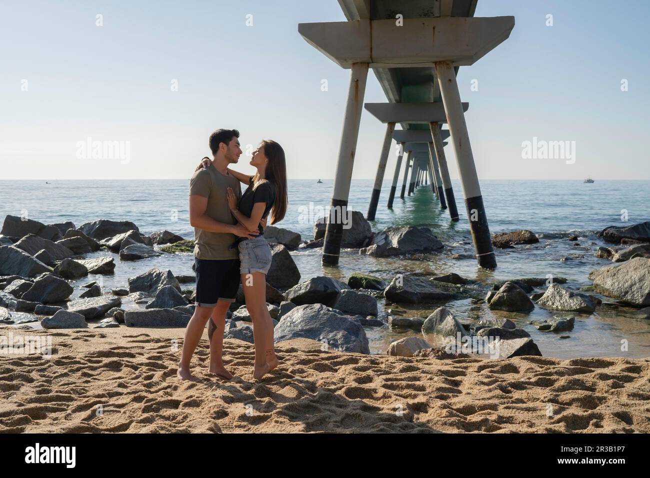 Giovane coppia in piedi insieme in spiaggia nelle giornate di sole Foto Stock