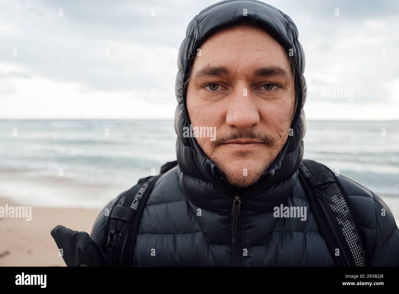 Uomo che indossa una giacca imbottita nera in spiaggia Foto Stock