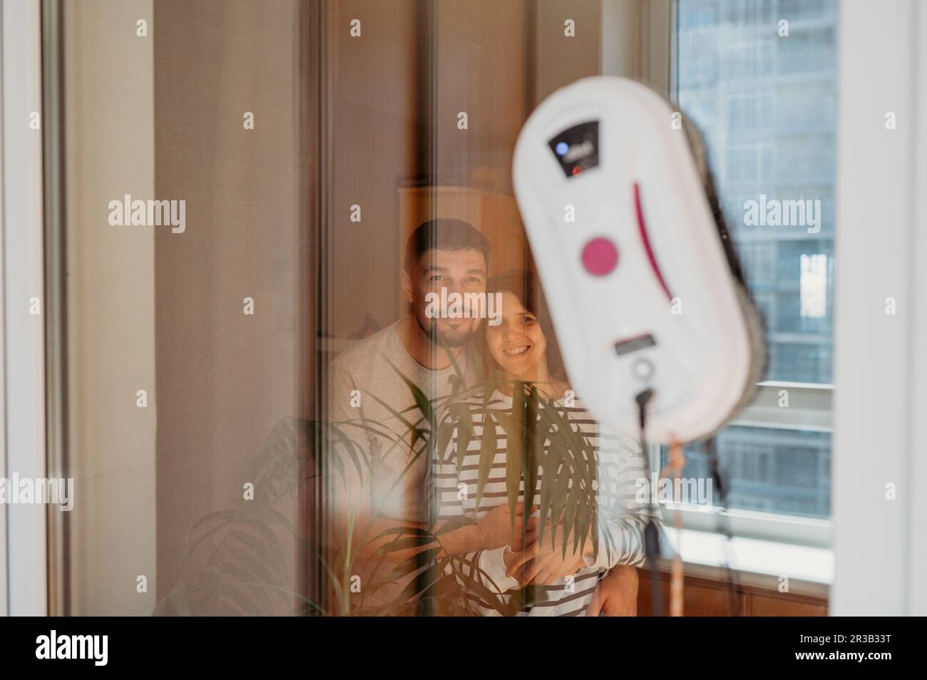 Coppia sorridente che guarda la finestra di pulizia del robot a casa Foto Stock