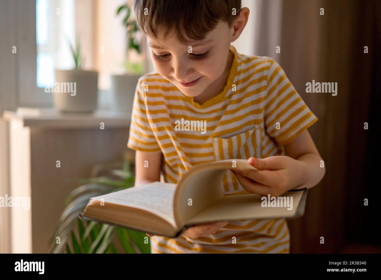 Ragazzo sorridente che capovolgerà le pagine del libro a casa Foto Stock