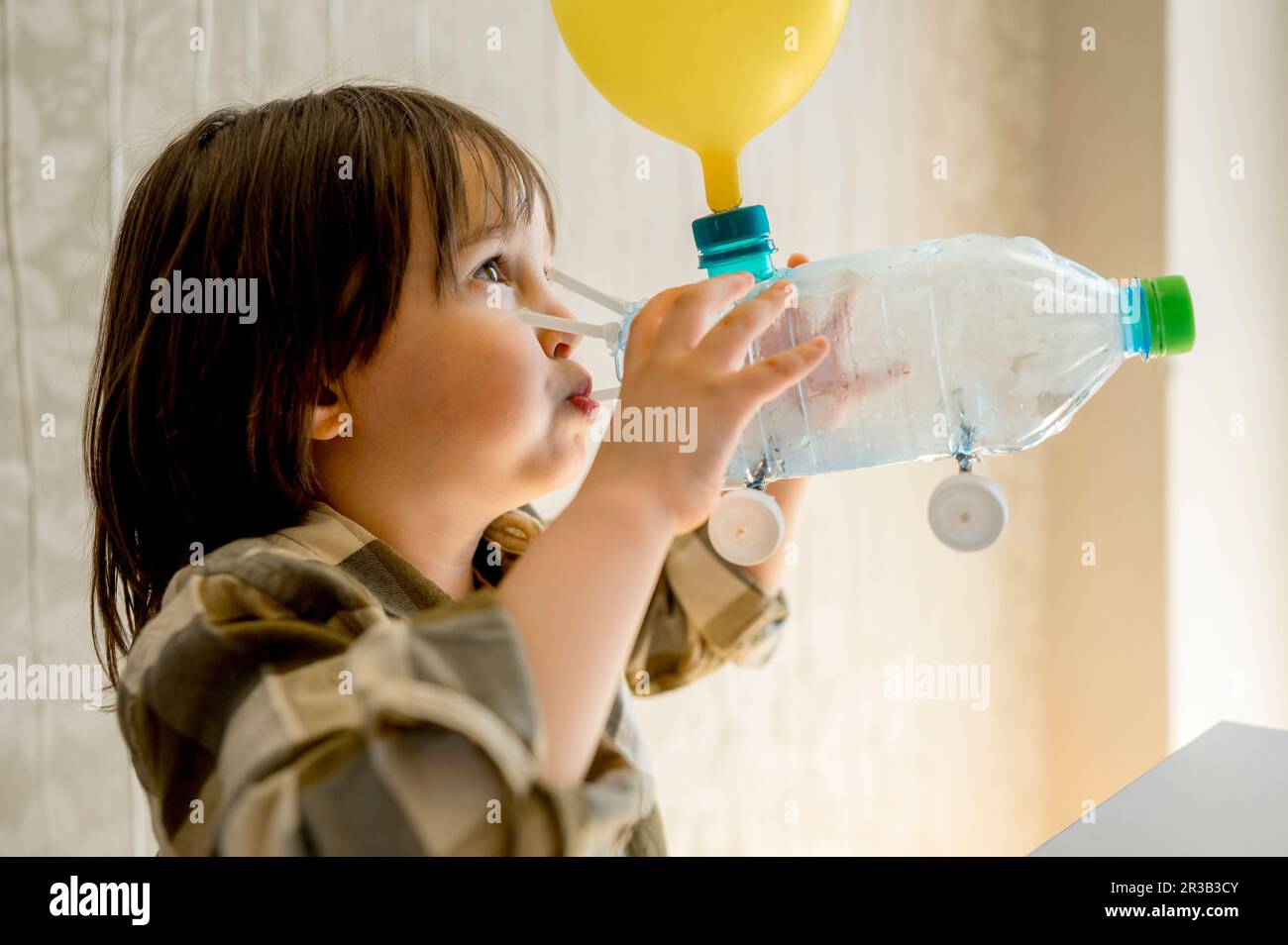 Il ragazzo che soffia il palloncino usando l'automobile della bottiglia di plastica a casa Foto Stock