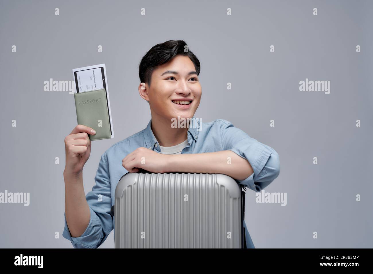 Ritratto di un giovane uomo sorridente che mostra il passaporto con il biglietto e si appoggia sulla valigia sopra il bianco Foto Stock