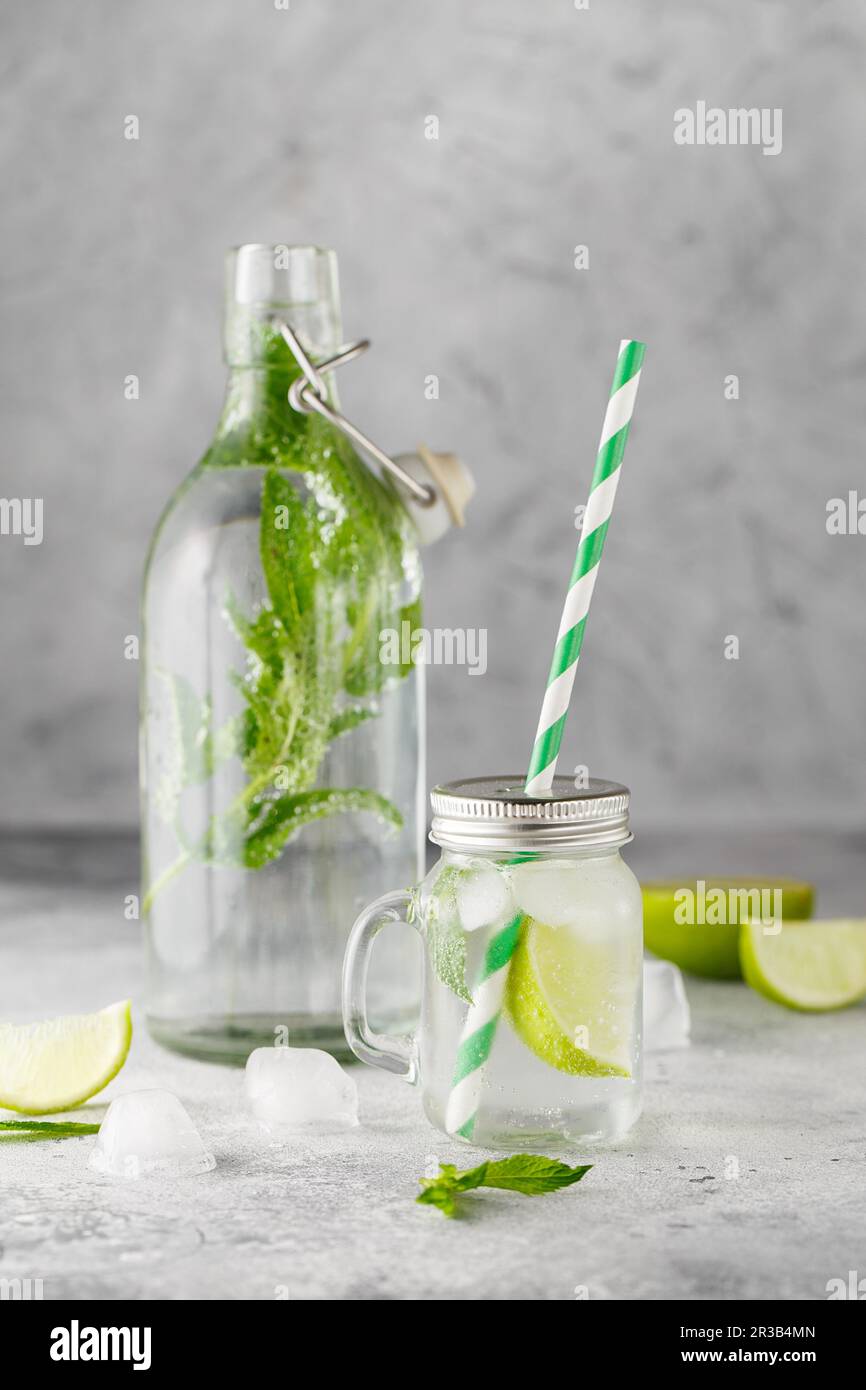 Bottiglia di vetro e vaso di limonata con limonata fredda con foglie di menta fresca e lime con cubetti di ghiaccio su g Foto Stock