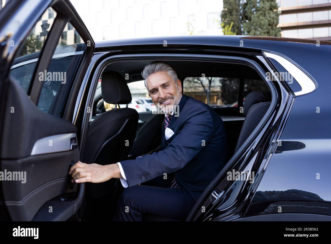 Un uomo d'affari sorridente che apre la porta posteriore dell'auto Foto Stock