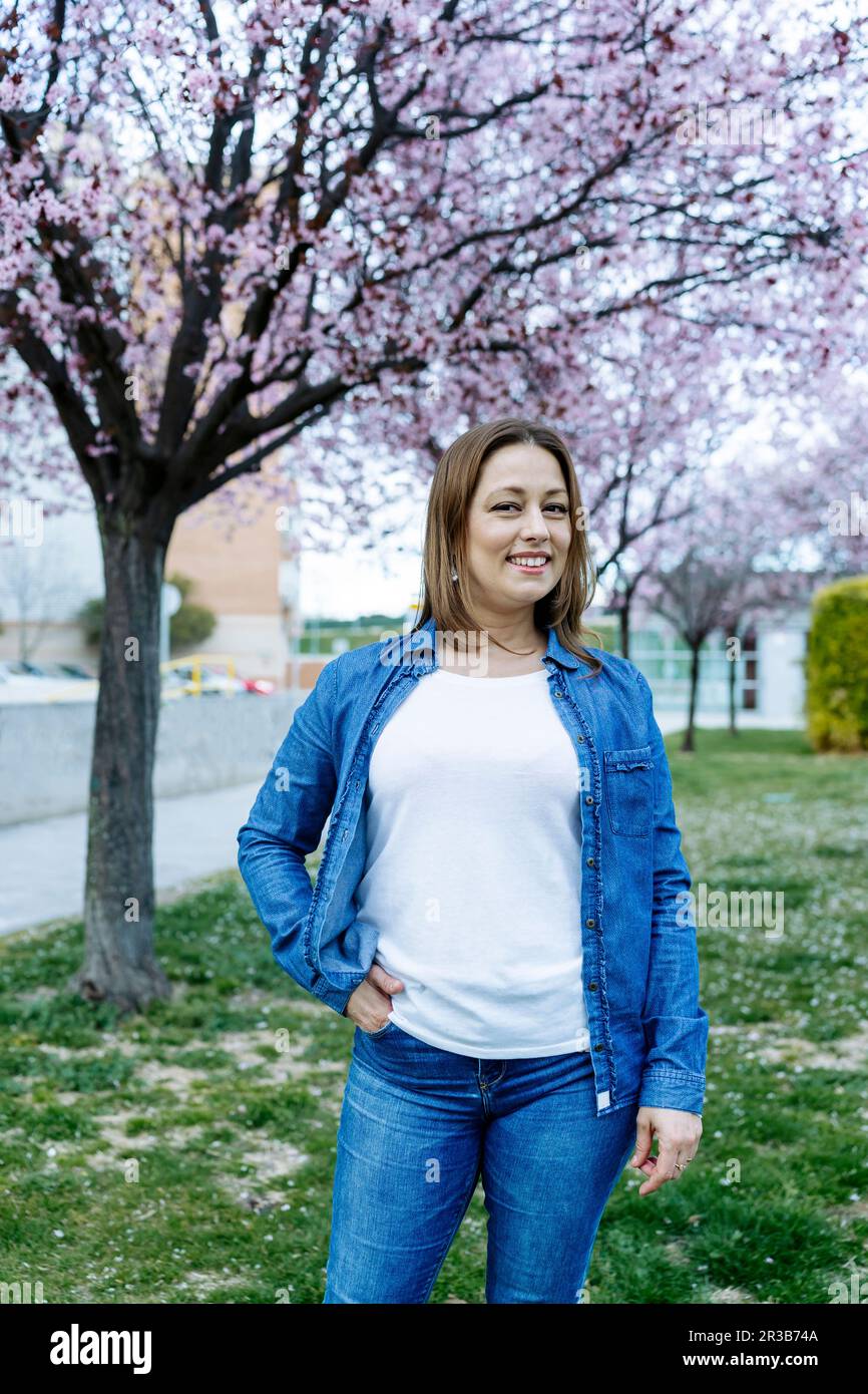 Donna sorridente con mano in tasca in piedi al parco Foto Stock