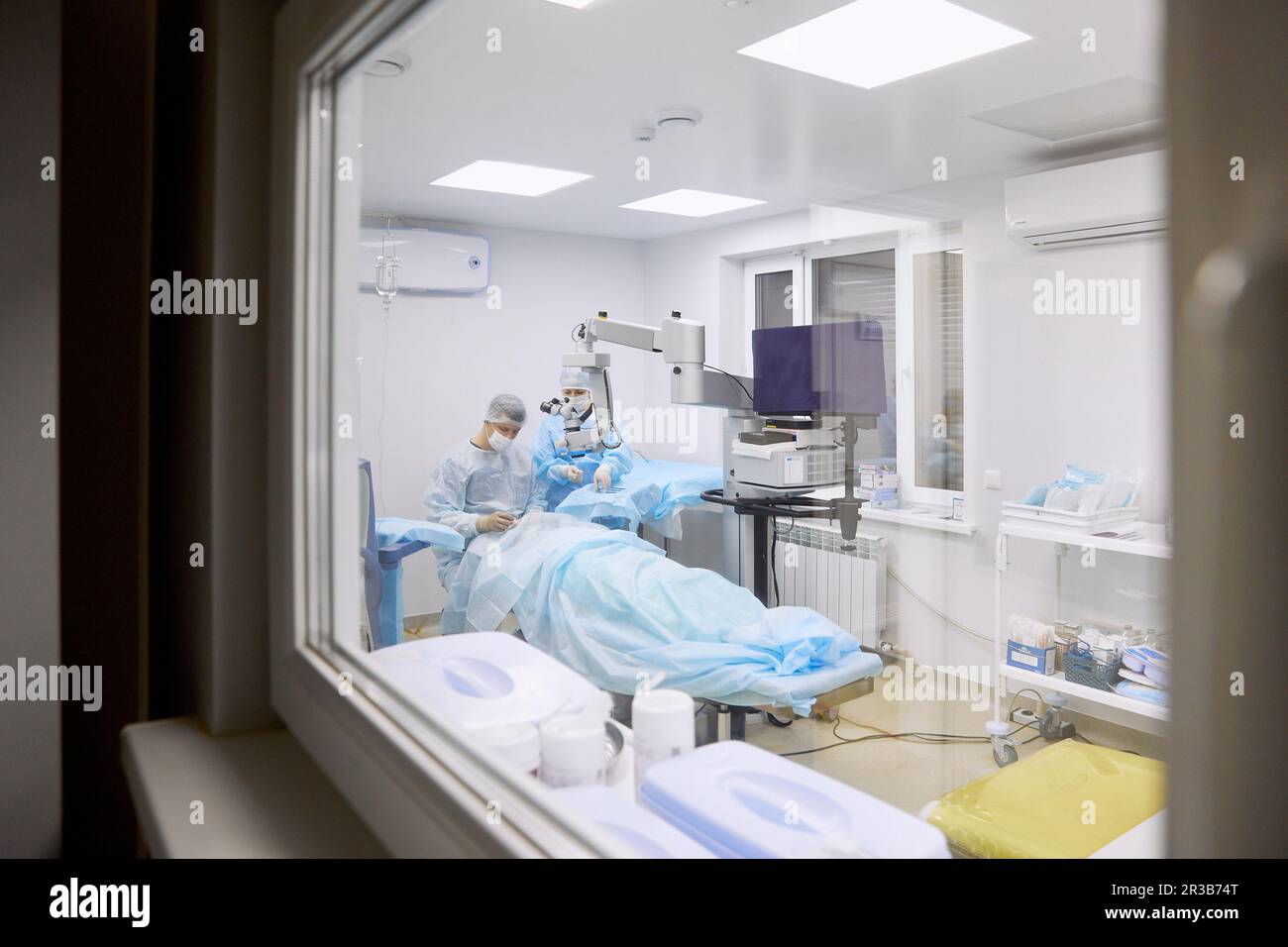Medico che esegue la chirurgia oculare in sala operatoria visto attraverso la finestra di vetro Foto Stock