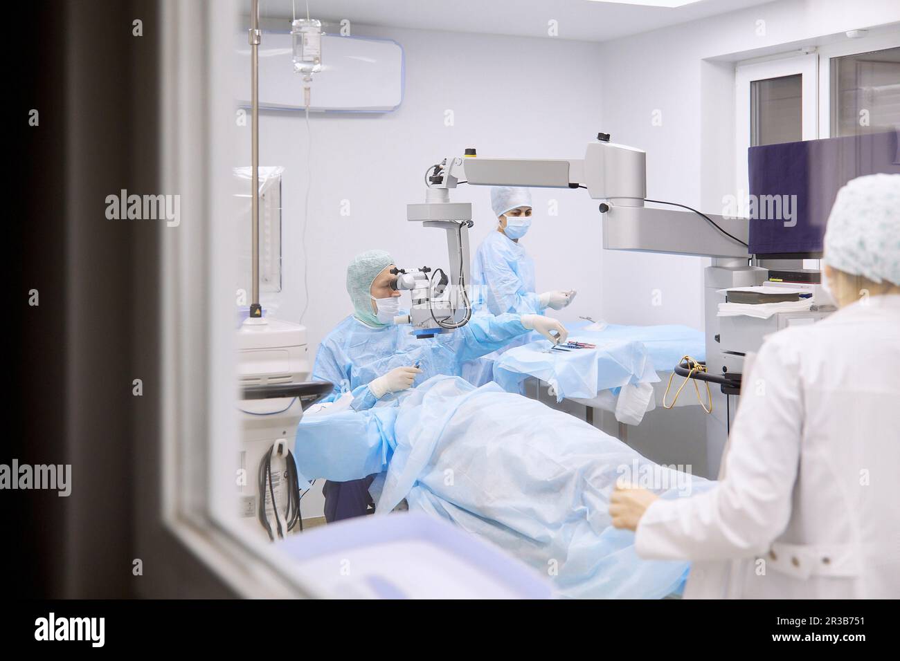 Oftalmologo che esegue chirurgia oculare in sala operatoria vista attraverso la finestra di vetro Foto Stock