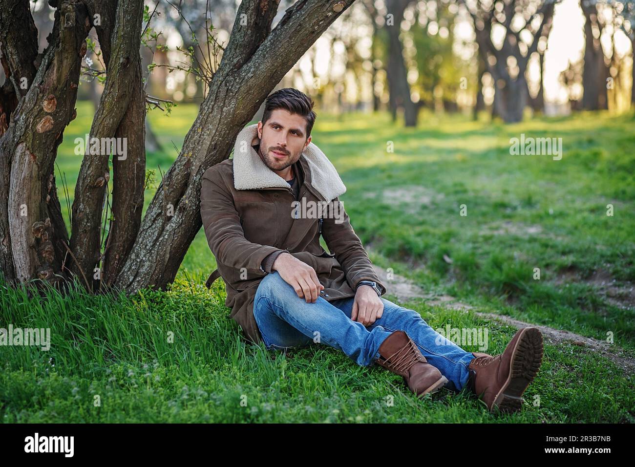 Ritratto di giovane attraente trendy seduto su erba verde in un parco al tramonto Foto Stock