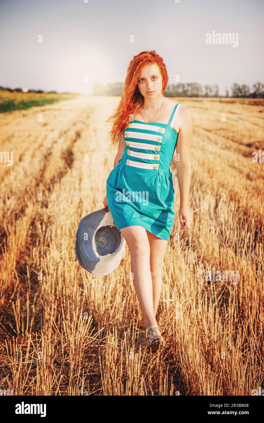 Ragazza capelli rossi godendo la natura nel prato. Bella donna in abito blu a piedi sul smussato, Sole Foto Stock