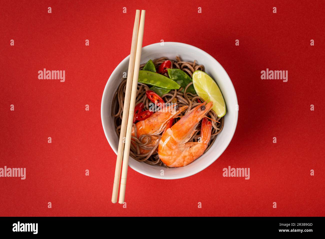 Gli spaghetti di soba asiatici mescolano con i gamberetti, le verdure, i piselli verdi, il pepe rosso in ciotola bianca con i chopsticks di legno Foto Stock