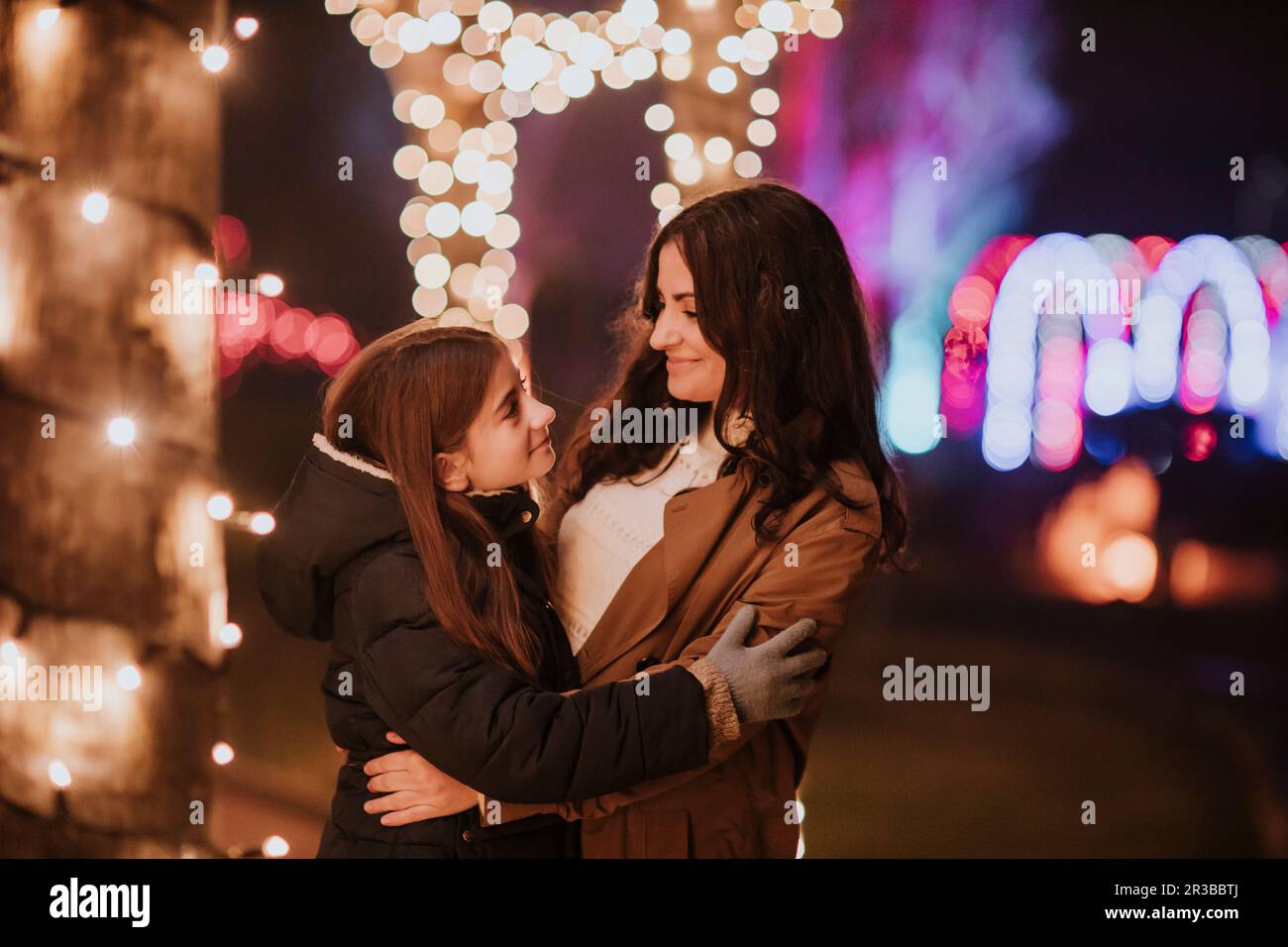 Donna sorridente che abbraccia figlia da luci illuminate Foto Stock