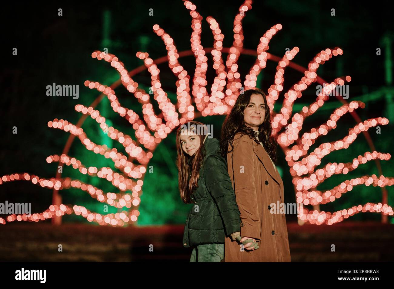 Sorridente madre e figlia in piedi indietro a indietro di fronte alle luci di Natale Foto Stock