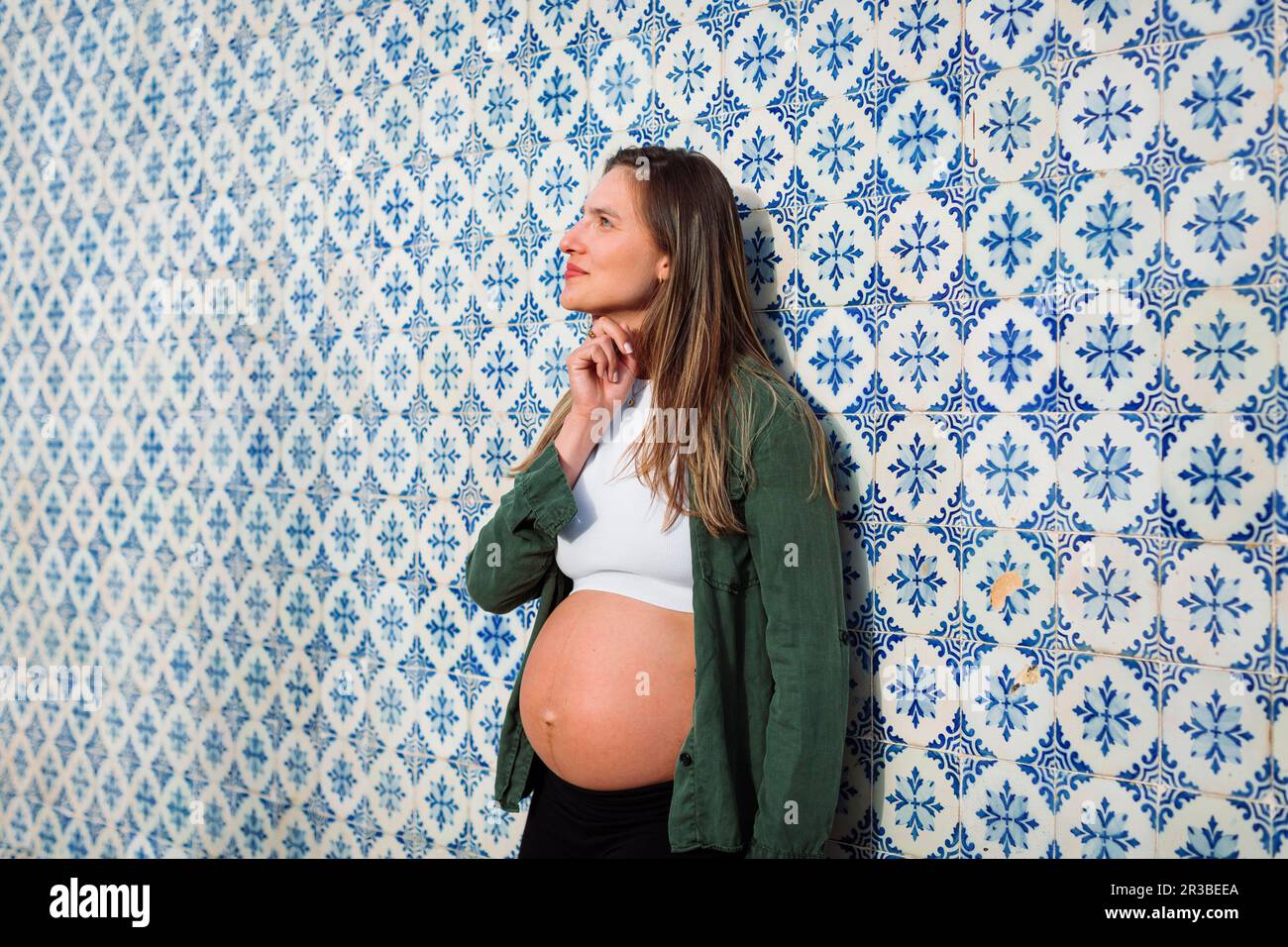 Donna incinta premurosa appoggiata su una parete piastrellata a motivi geometrici Foto Stock