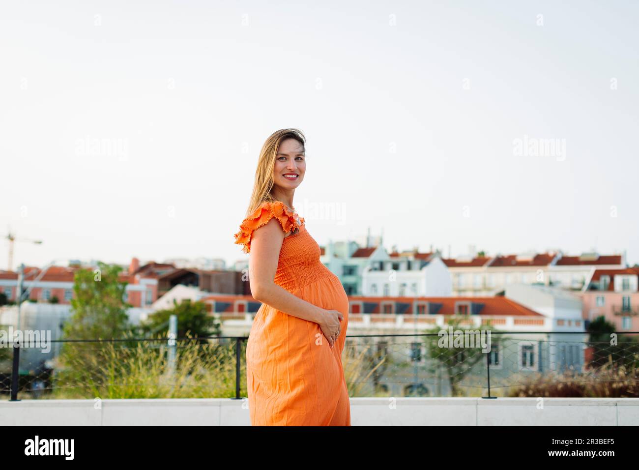 Donna incinta sorridente che indossa un abito arancione Foto Stock