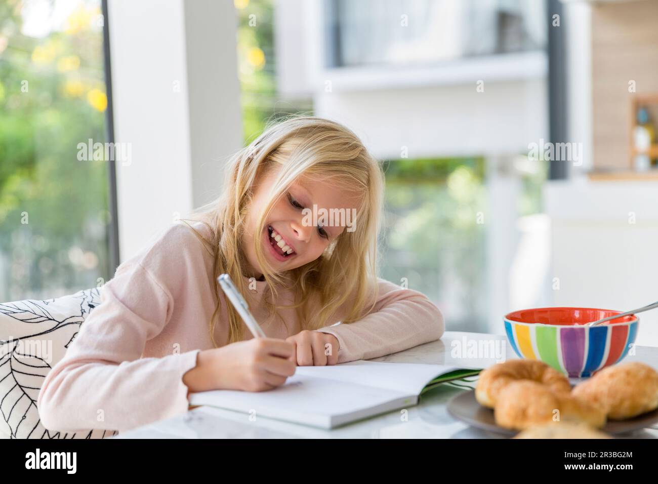 Ragazza bionda sorridente che fa i compiti a casa Foto Stock