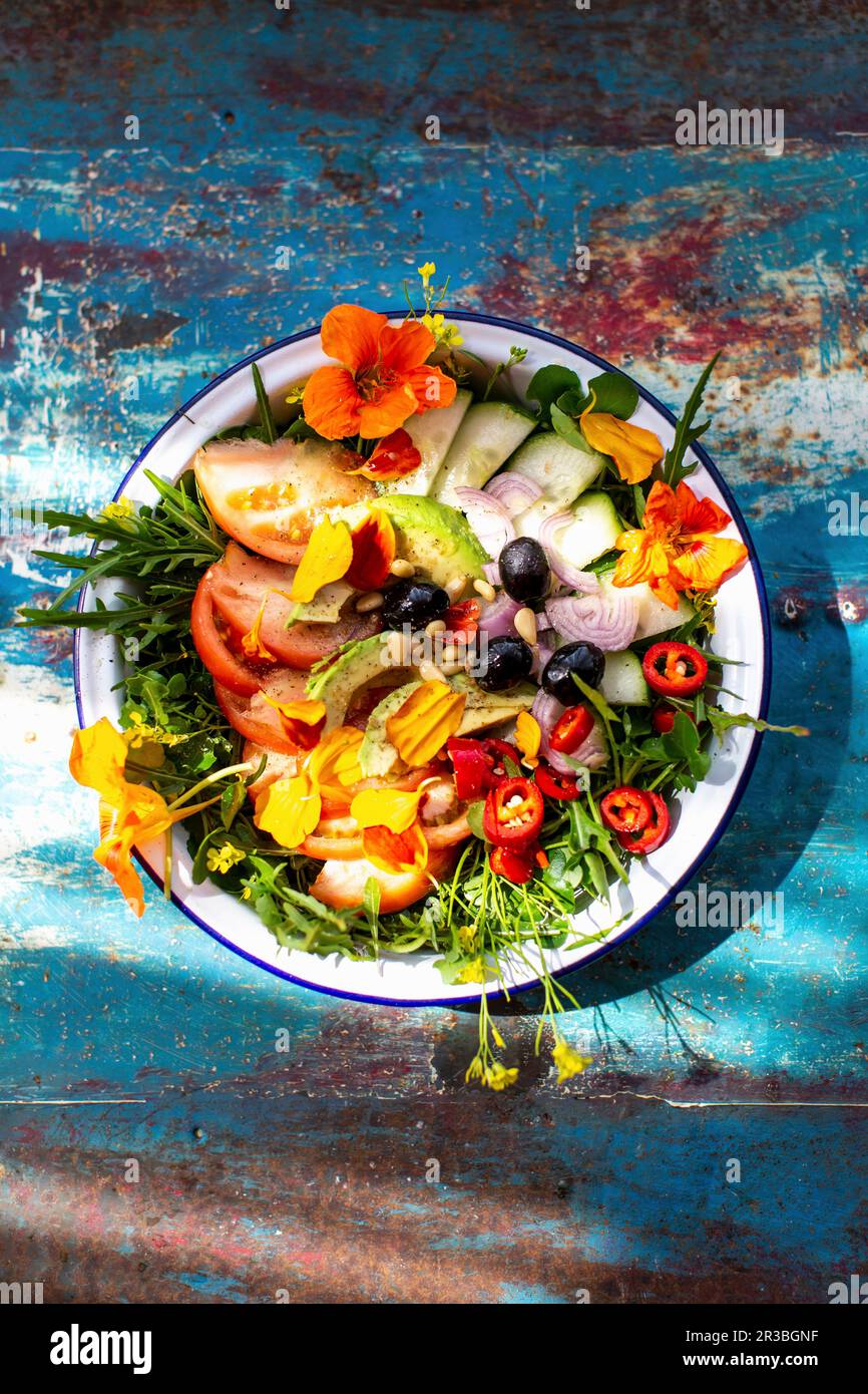 Insalata estiva con pomodori, cetriolo, peperoncino, olive e fiori commestibili Foto Stock