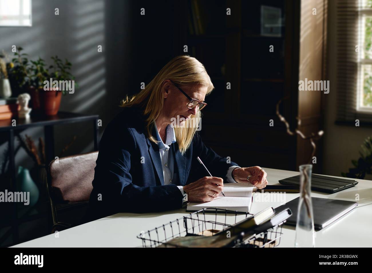 Psicologo biondo senior che prepara appunti alla scrivania in ufficio Foto Stock