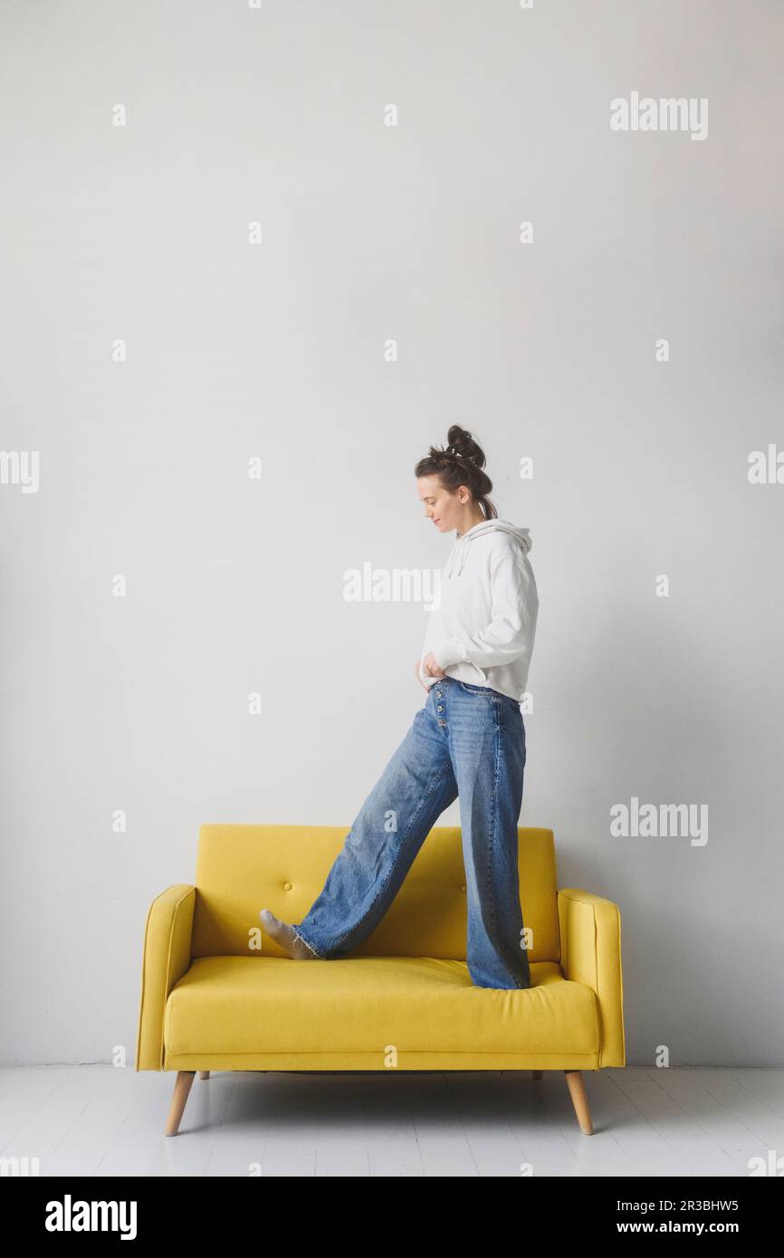 Donna vestita con abbigliamento casual che cammina sul divano giallo Foto Stock