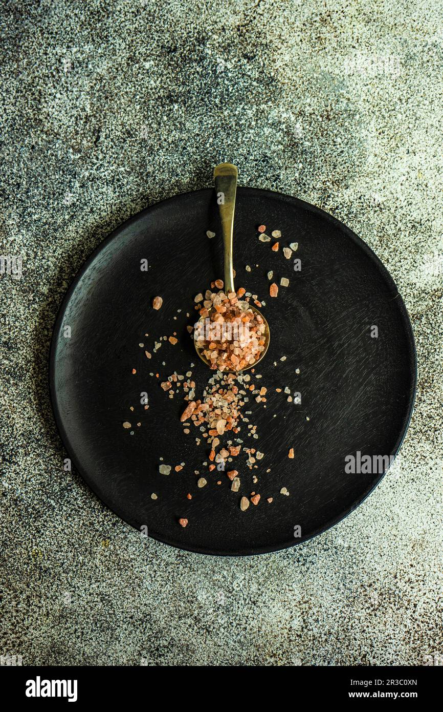 Cucina con cucchiaio d'annata con sale rosa su piatto di legno nero Foto Stock