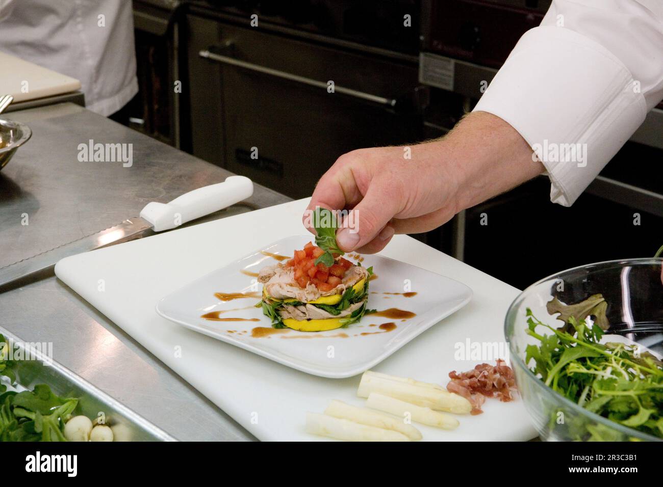 Mano dello chef che aggiunge la decorazione ad un piatto in una cucina del ristorante Foto Stock