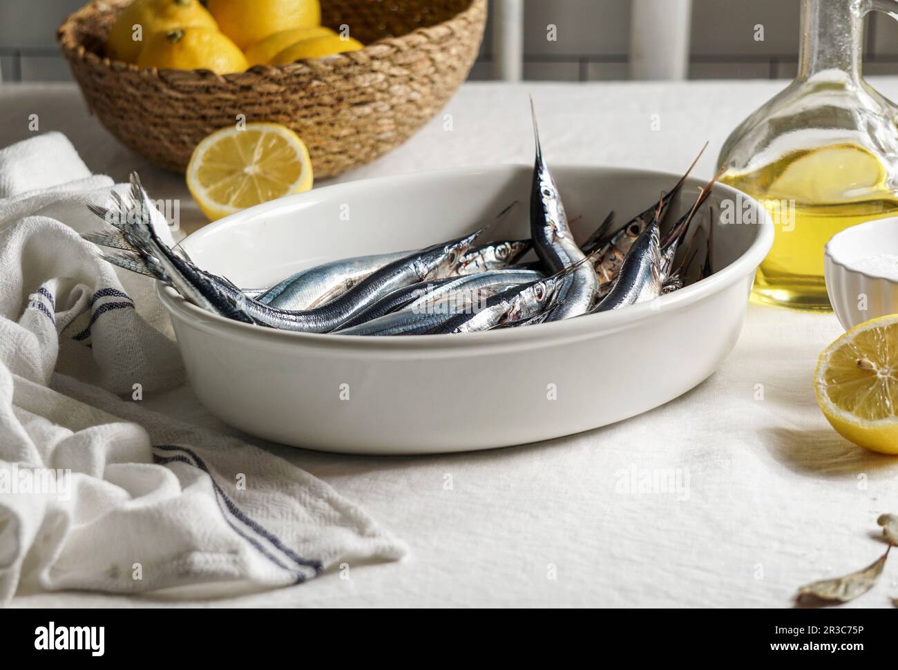 Pesce ago fresco, sardine sul tavolo da cucina, tovaglia di lino, limoni e sale Foto Stock