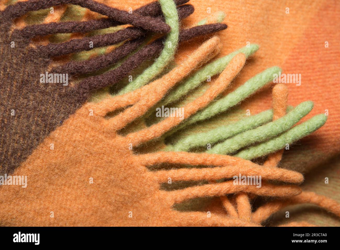 Coperta morbida e calda in lana d'alpaca ripiegata con frangia. Macrofo a trama di lana verde e arancione Foto Stock