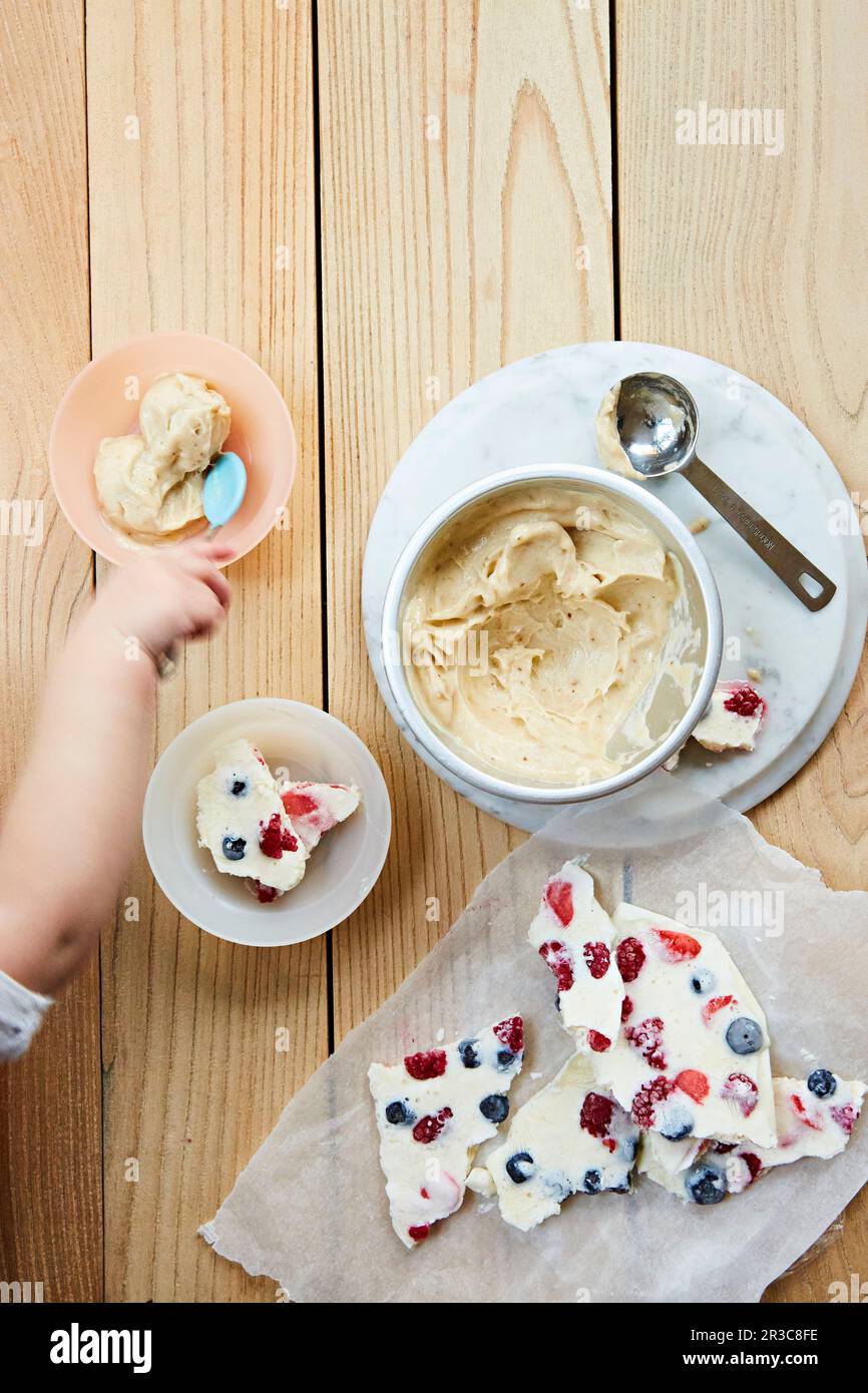 Shards di frutta e gelato per bambini. Una mano del bambino che arriva con un cucchiaio Foto Stock
