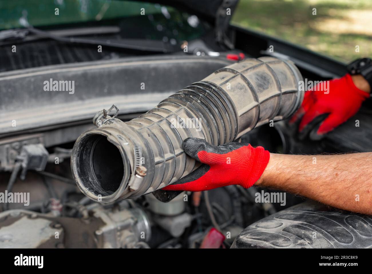 Un meccanico auto tiene in mano un tubo pneumatico scollegato dal motore di un'auto. Riparazione auto. Foto Stock