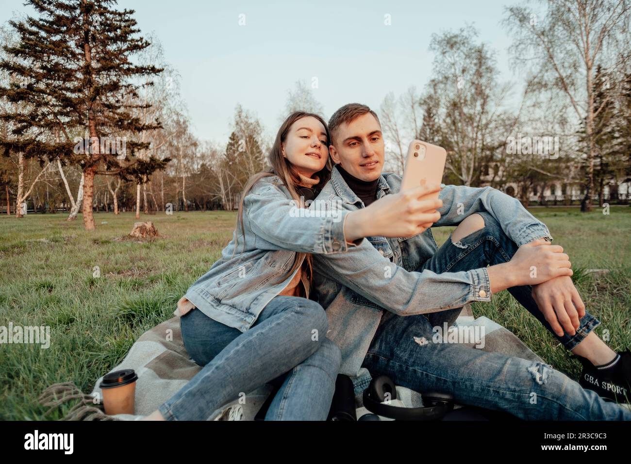 giovane coppia alla moda sorride guardando il telefono nel parco, selfie Foto Stock