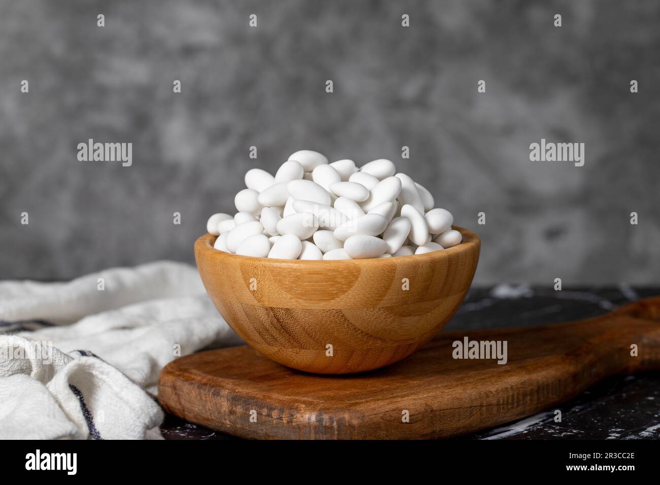 Caramelle alle mandorle. Caramella di mandorle ricoperta di zucchero in una ciotola di legno su fondo scuro. Piccole caramelle multicolore Foto Stock