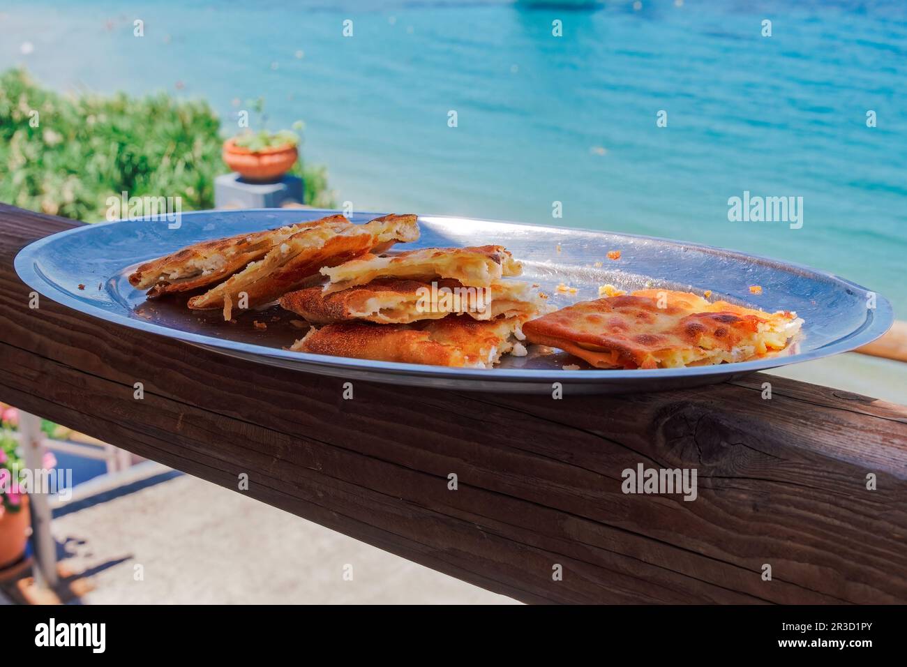 Un piatto con tiropita greca, porzioni di torta di formaggio feta con strati di pasta fillo imburrata sullo sfondo di un mare sfocato. Foto Stock