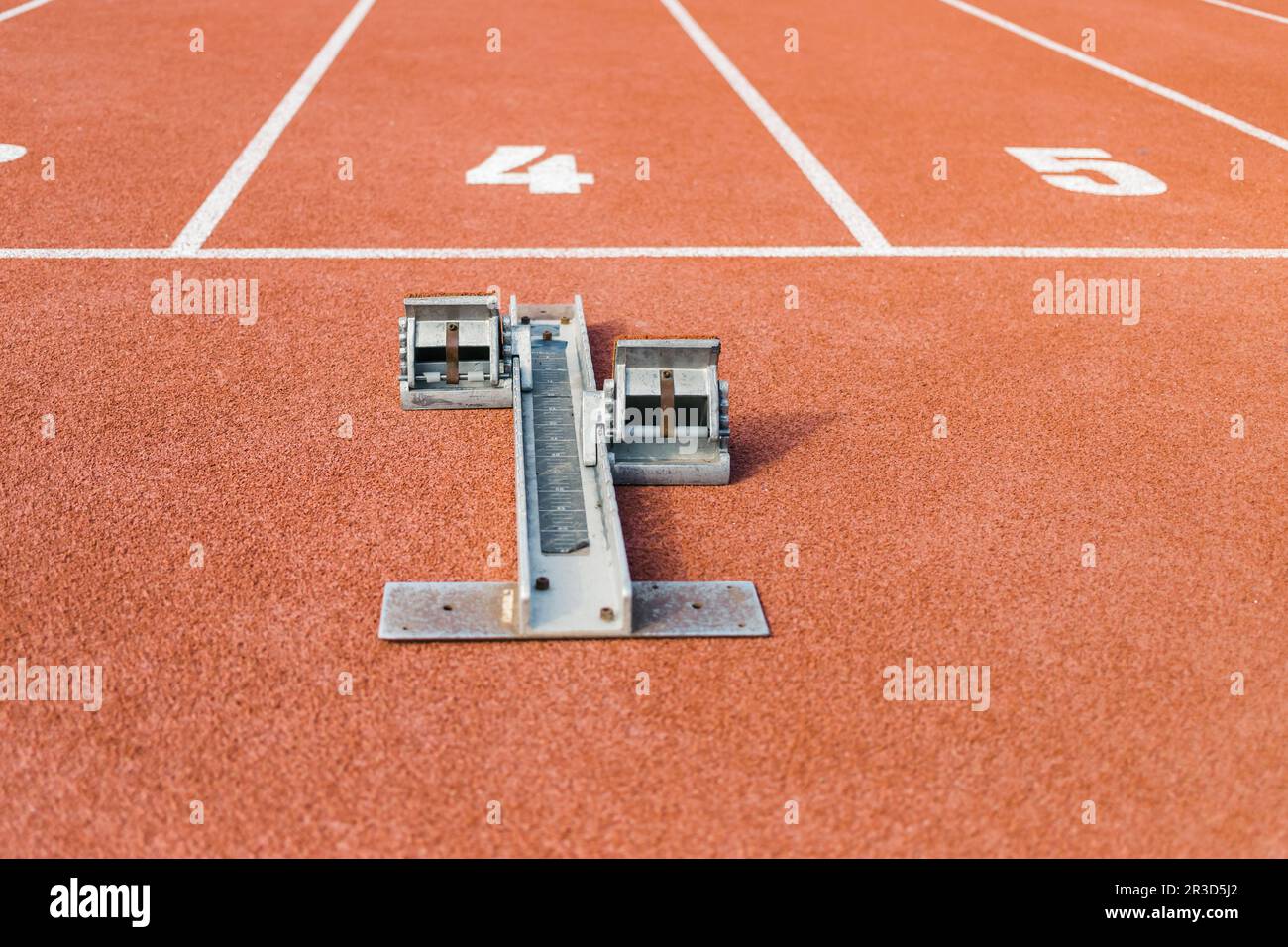 Superficie della pista di corsa con texture rosse con un blocco di partenza davanti alla linea di partenza numero quattro, primo piano a livello del suolo. Foto Stock