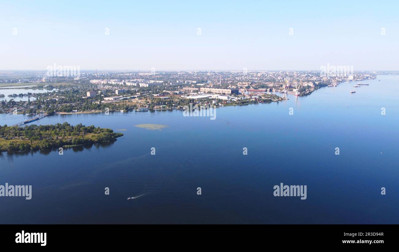 Il drone sorvola il fiume ondeggiante circondato dalla città industriale con vari edifici e Wetland e mar Foto Stock