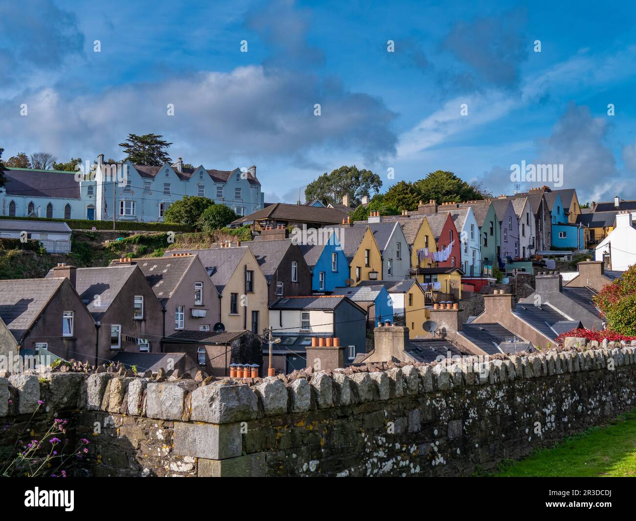 Case europee multicolore lungo la strada della piccola città irlandese di Cobh, paesaggio urbano. Cielo blu sulla città. Case sotto il cielo blu Foto Stock