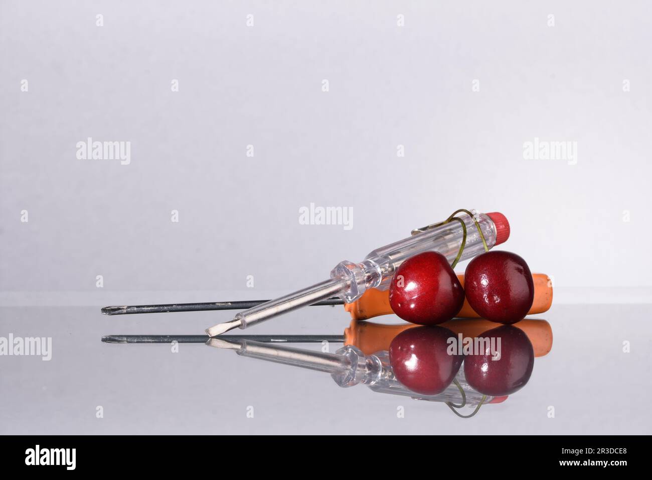 coppia di cacciaviti con due ciliegie rosse per rappresentare il concetto di lavorare dolcemente in modo insolito Foto Stock