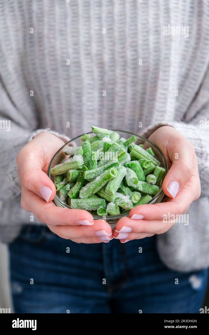 Recipiente per tenere le mani femminili con fagioli verdi congelati. Conservazione vegetale. Raccolto. Veganismo, alimentazione vegetariana sana. Foto Stock