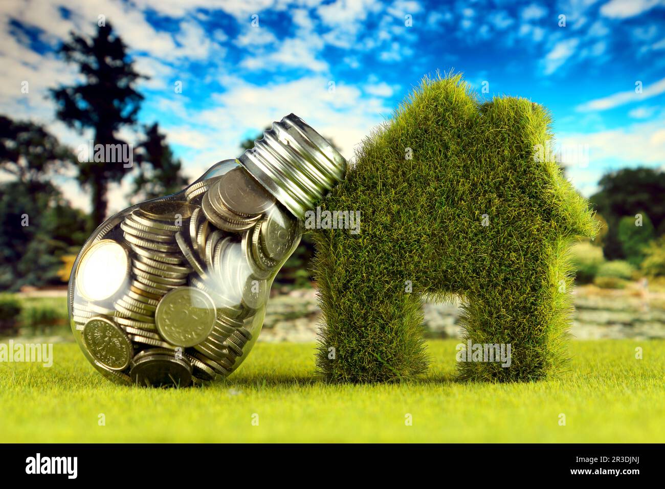 Monete all'interno della lampadina e casa in miniatura con erba. Eco-verde energia rinnovabile concetto. I prezzi dell'elettricità, il risparmio energetico in famiglia. Foto Stock