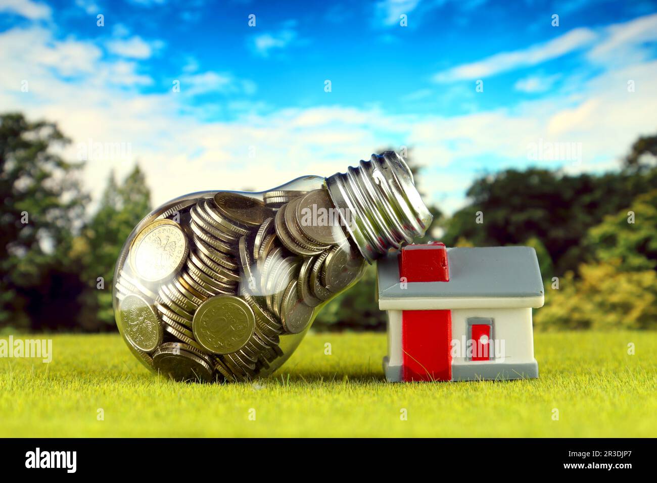 Monete all'interno della lampadina e casa in miniatura sull'erba. Eco-verde energia rinnovabile concetto. I prezzi dell'elettricità, il risparmio energetico in famiglia. Foto Stock